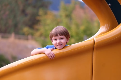 Bambino che sorride su uno scivolo giallo.