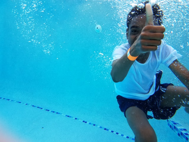 Bambino a una festa in piscina che saluta facendo il pollice in su.