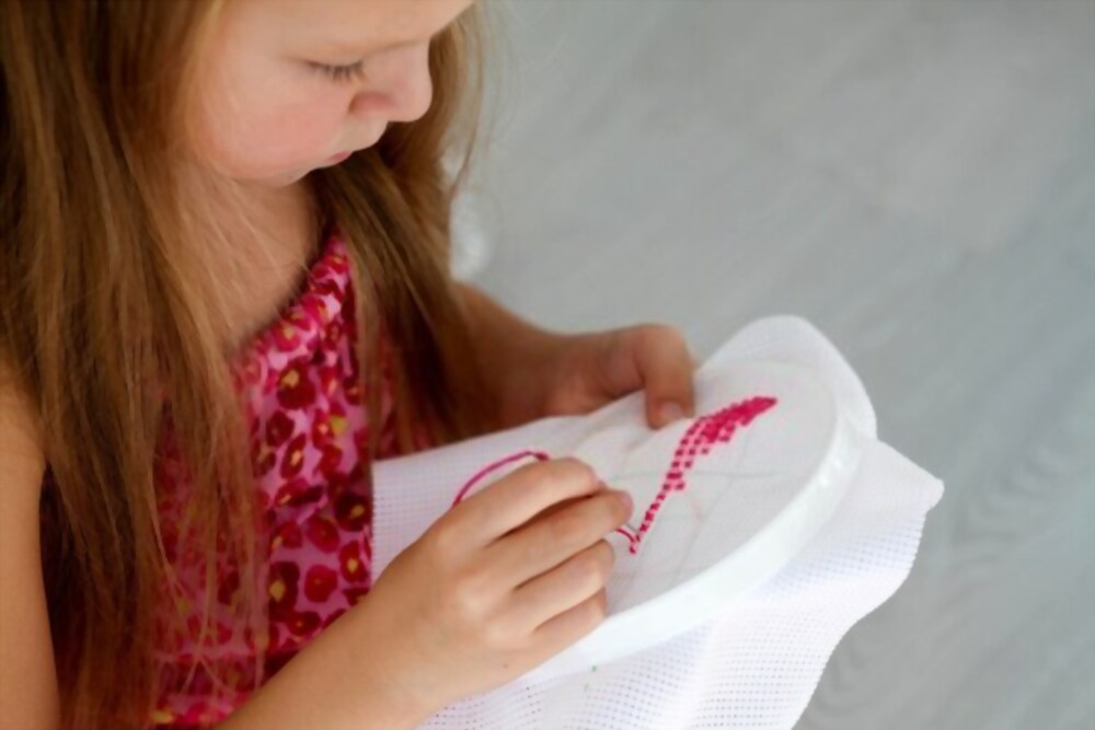 Bambina che ricama uno schema a punto croce durante un laboratorio sartoriale