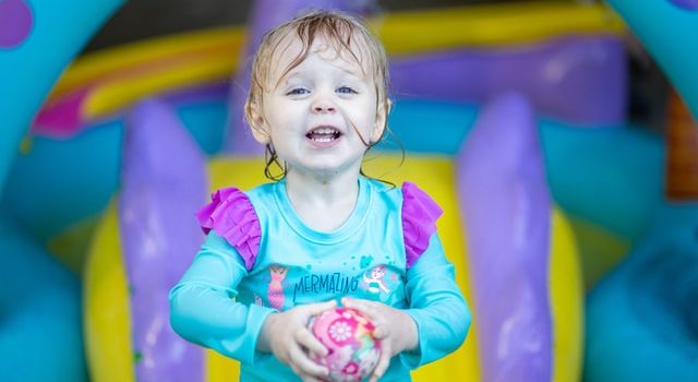 bambina con una palla in mano di fronte ad un gonfiabile, affittato tramite un servizio di noleggio gonfiabili