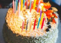 torta di compleanno con candeline accese e scritta happy birthday