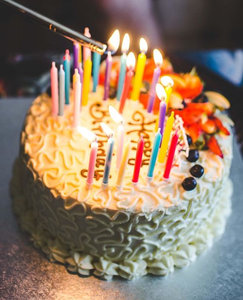 Torta di compleanno con candeline accese e scritta "happy birthday"
